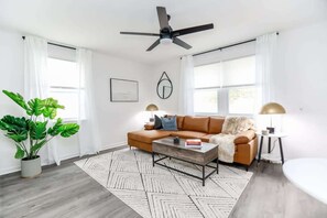 Ein modernes Wohnzimmer mit einem Ecksofa, einem Couchtisch, einem Deckenventilator und einer Zimmerpflanze.