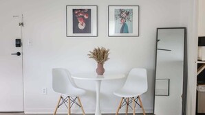 A room with a white round table, two white chairs, a vase with dried plants, and two framed artworks on the wall. - Sojourn | The South Shore Apartments (Norfolk)