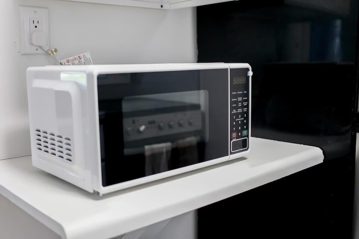 Un microondas blanco sobre una encimera blanca, con un horno negro al fondo.