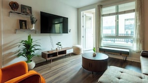 Un salon moderne doté d’un téléviseur à écran plat, de parquet, d’une table basse ronde et d’un banc placé près de la fenêtre.