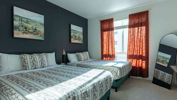 A bedroom with two beds, a window with red curtains, and two paintings on the wall. - Modern Serenity Apt for a Comfortable Stay (Glendale)