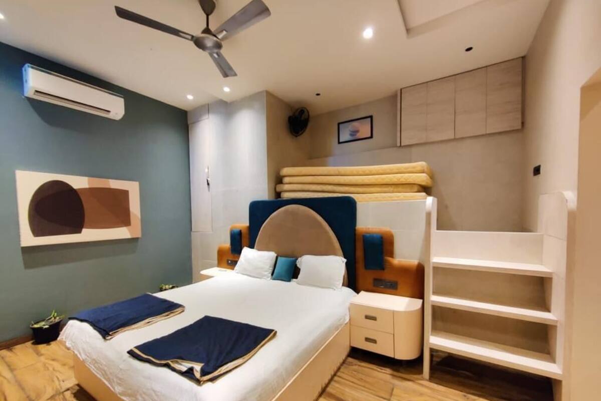 A modern hotel room with a large bed, a ceiling fan, a built-in shelf unit, and a wall-mounted air conditioner.