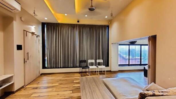 A modern hotel room with a wooden floor, a bed, a bench, and a view of the city through large windows.