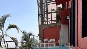 A clear swimming pool with a tiled deck, surrounded by palm trees and a red building with large windows.