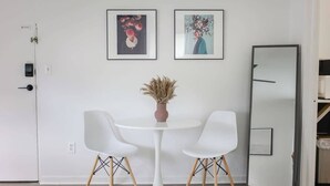 Et værelse med et rundt, hvidt bord, to hvide stole, en vase med tørrede planter og to billeder i rammer på væggen.