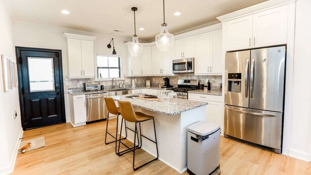 A modern kitchen with white cabinets, stainless steel appliances, and a central island with bar stools. - Sojourn | EastBay Gateway with Game Room (Norfolk)