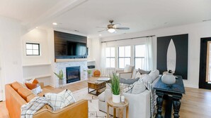 A modern living room with a fireplace, a ceiling fan, and a large window. - Sojourn | EastBay Gateway with Game Room (Norfolk)