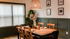 A dining area with a wooden table, four chairs, a hanging light fixture, and framed pictures on the wall. - Sojourn | EastBay Gateway with Game Room (Norfolk)