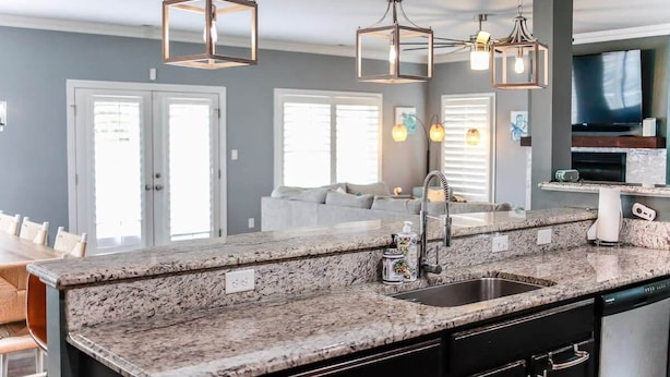 Una cucina moderna con piani in granito, lavello in acciaio inossidabile e illuminazione a sospensione.