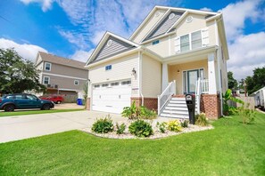 A two-story house with a garage, a front porch with steps, and a well-maintained lawn. - Sojourn Baycation Beach House 5 Min Walk to Beach (Norfolk)