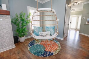 A room with a hanging chair, a potted plant, and a colorful rug. - Sojourn Baycation Beach House 5 Min Walk to Beach (Norfolk)