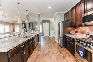 A modern kitchen with dark wood cabinets, stainless steel appliances, and a granite countertop. - Sojourn Baycation Beach House 5 Min Walk to Beach (Norfolk)