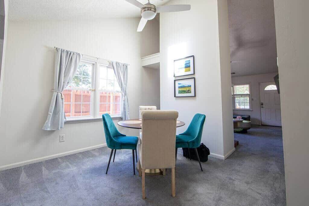 A dining area with a round table and two chairs, a ceiling fan, and a window with curtains.