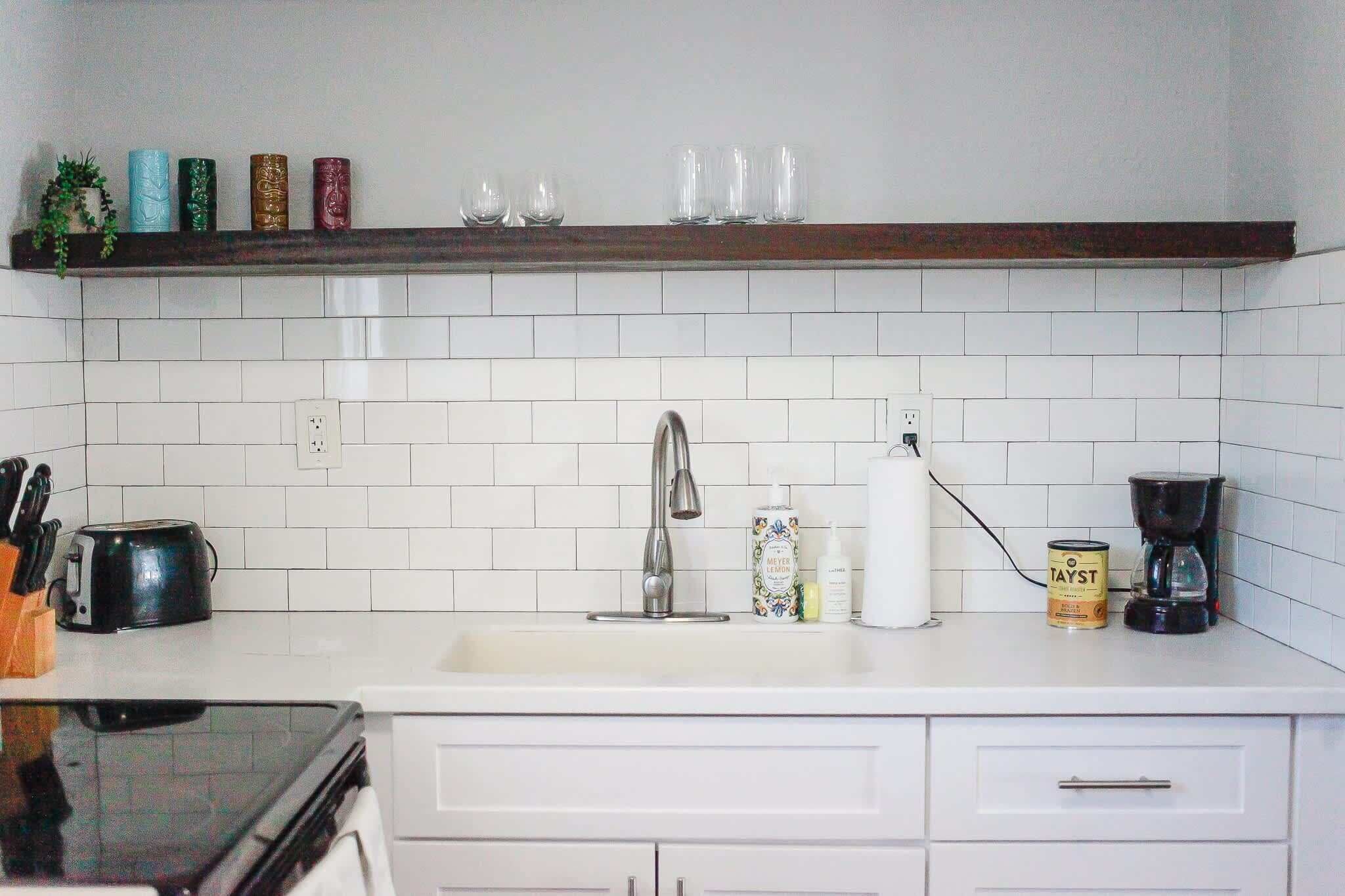A kitchen with white cabinets, a stainless steel sink, a coffee maker, and a shelf with decorative items.