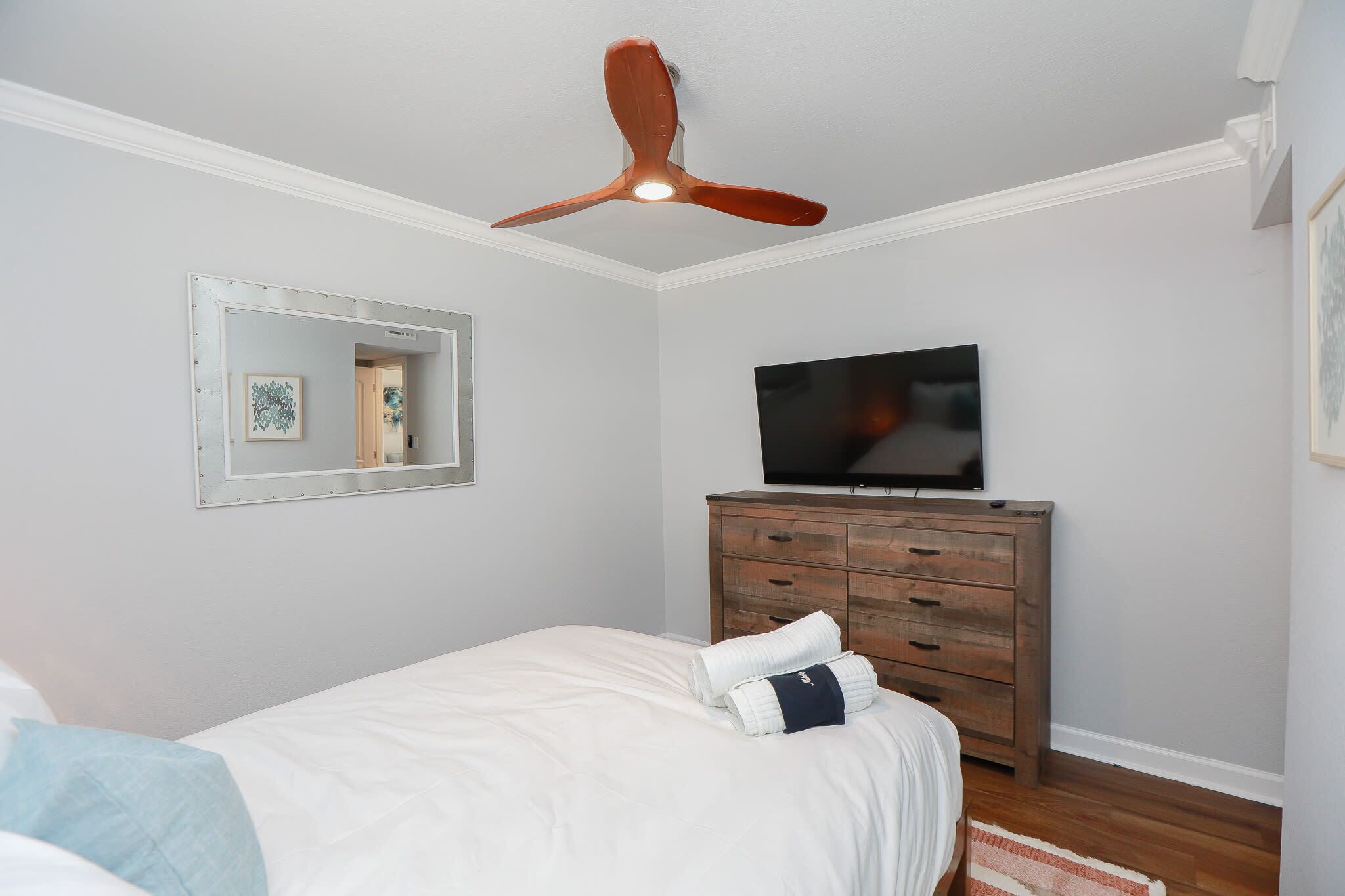 Un dormitorio con cama, cómoda, televisor, ventilador de techo y espejo.