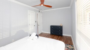 Ett sovrum med en säng, en byrå, en takfläkt och ett fönster med persienner.