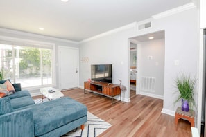 Una sala moderna con un conjunto de sofás, una mesita de centro, un televisor sobre un mueble de madera y una planta.