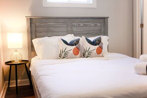 A neatly made bed with white bedding and decorative pillows featuring a nature-inspired design. - Sojourn Tide Suite 2 BR 2 BA at Beach Cottages (Norfolk)
