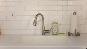 A kitchen sink with a modern faucet, a dish soap bottle, a hand soap bottle, and a paper towel holder. - Sojourn Cove Suite 2 BR 2 BA at Beach Cottages (Norfolk)
