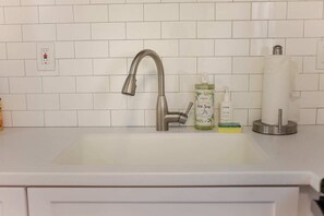 Ein Küchenspülbecken mit modernem Wasserhahn, einer Flasche Geschirrspülmittel, einer Handseifenflasche und einem Papiertuchhalter.