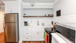 A modern kitchen with white cabinetry, a stainless steel refrigerator, a microwave, and a stove. - Sojourn's Tide Suite at Beach Cottages (Norfolk)