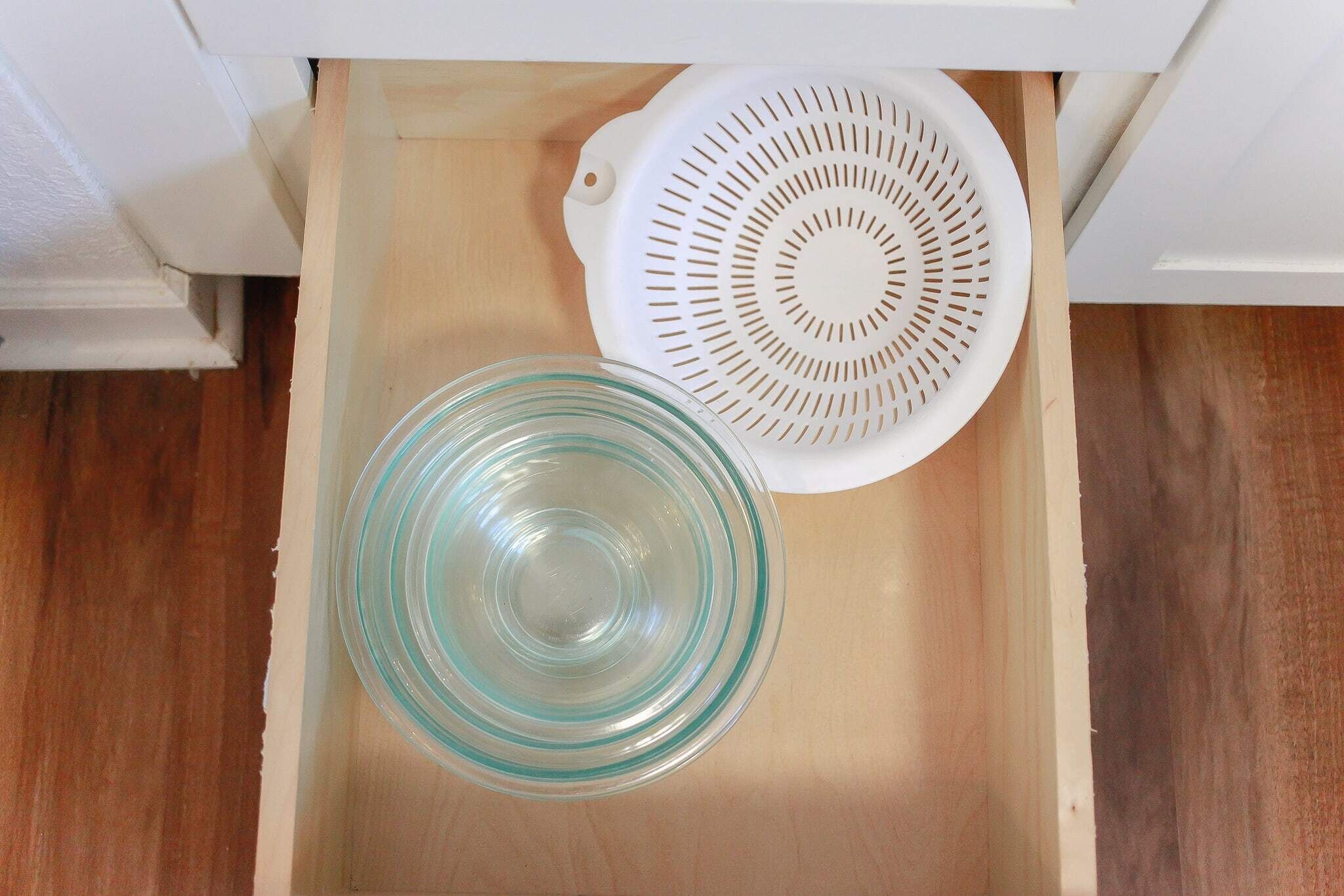 Un tiroir de cuisine contenant une passoire blanche et un saladier en verre transparent.