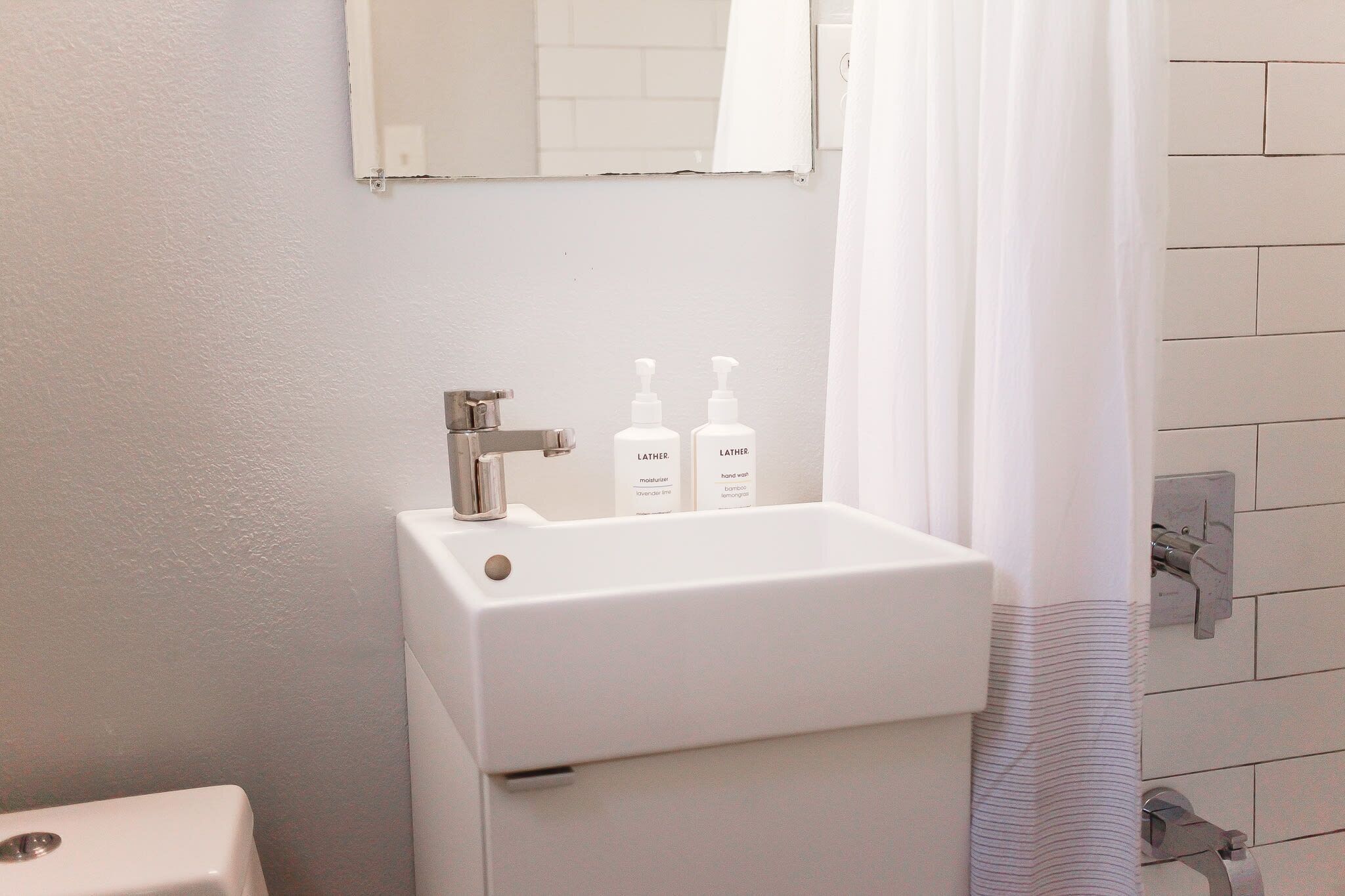Un bagno con un lavandino bianco, due flaconi di sapone per le mani LATHER e una tenda da doccia.