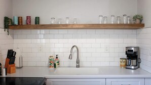 Ett kök med ett vitt kakel som stänkskydd, en kran i rostfritt stål, en kaffebryggare och en hylla med glasburkar.