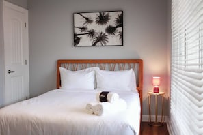 A neatly made bed with white linens, a headboard, and a wall-mounted artwork. - Sojourn Tide Suite 2 BR 2 BA at Beach Cottages #11 (Norfolk)