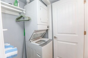 Een kleine wasruimte met een voorlader wasmachine en droger, een witte deur en een handdoekrek met blauwe en witte handdoeken.