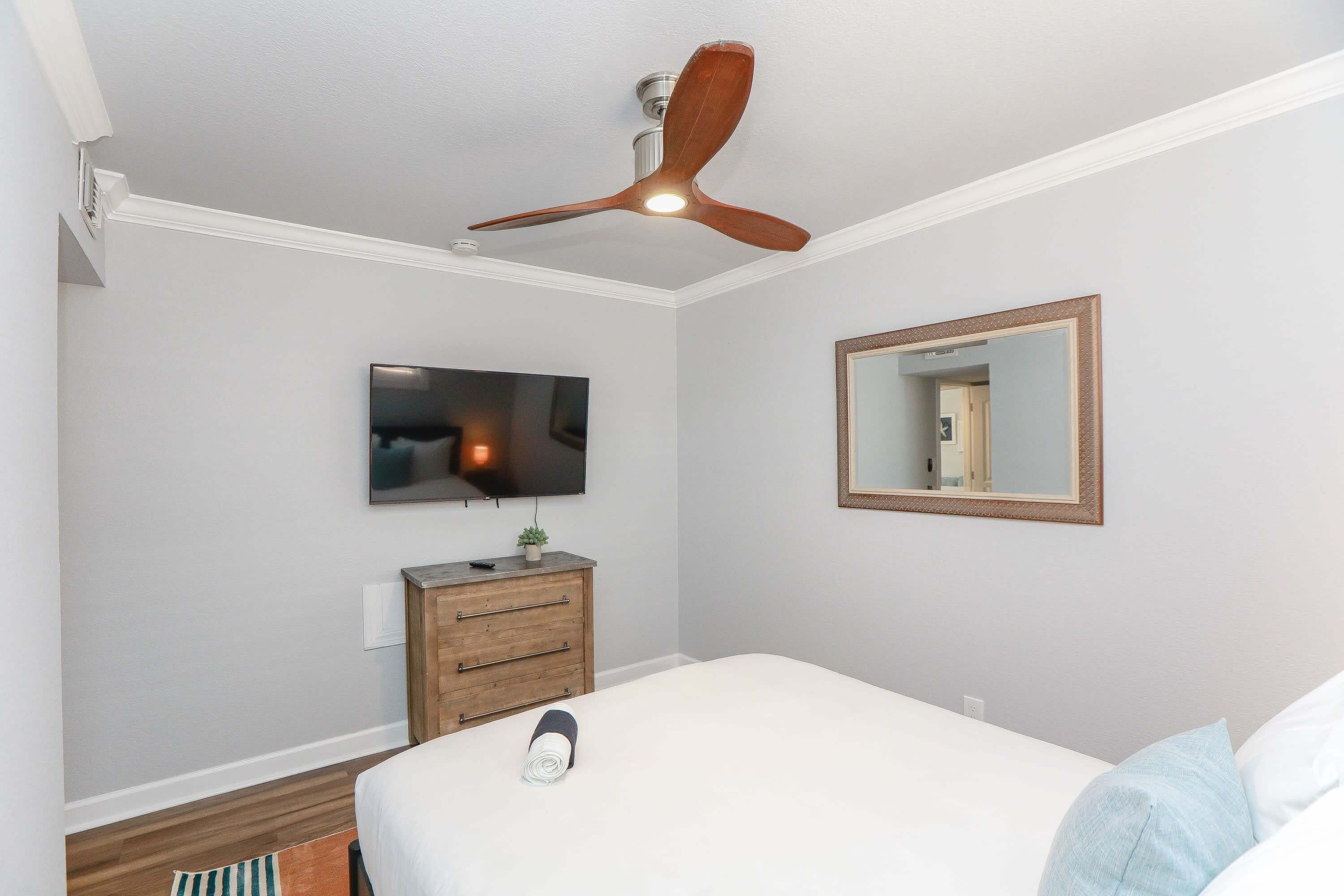 Un dormitorio con cama, ventilador de techo, televisor, cómoda y espejo.