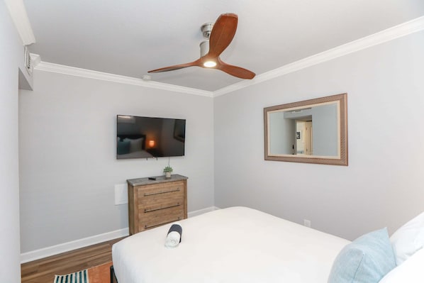 Een slaapkamer met een bed, een plafondventilator, een televisie, een dressoir en een spiegel.