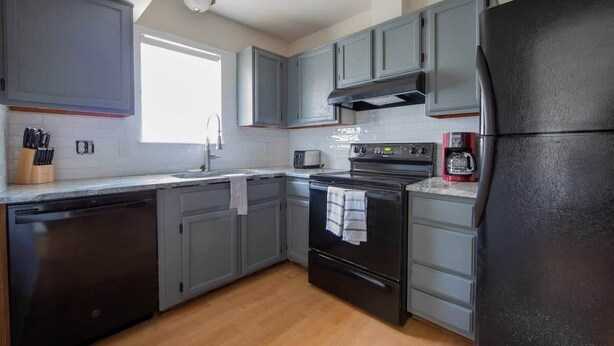 A kitchen with grey cabinets, a black refrigerator, a stove, and a dishwasher. - Sojourn | Virginia Beach | 2 Bedroom Townhouse (Virginia Beach)