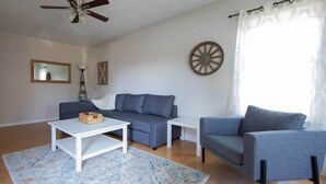 A living room with a ceiling fan, a sofa, a chair, and a coffee table. - Sojourn | Virginia Beach | 2 Bedroom Townhouse (Virginia Beach)