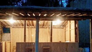 A covered outdoor area with a wooden bench and a table, bamboo walls, and a pergola with lights. - Angel Eco Resort & Restaurant Cox'sBazar (Cox's Bazar)