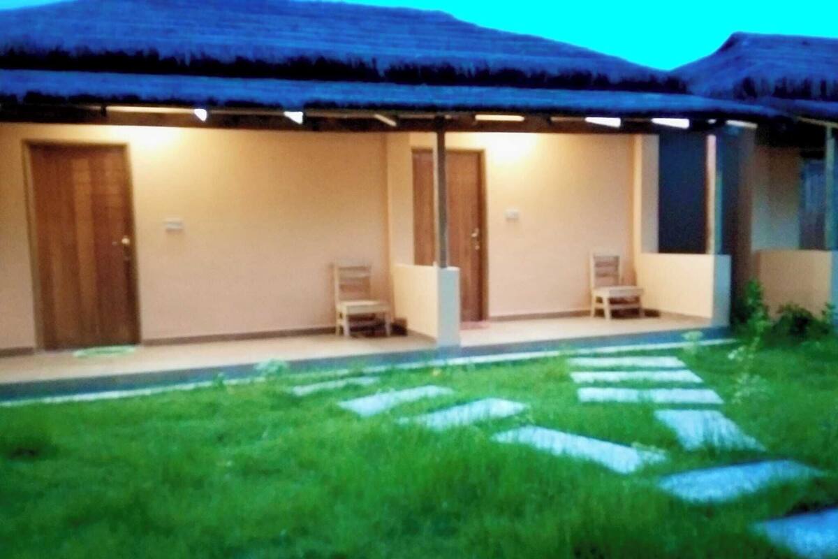 A two-story building with a thatched roof, a covered porch with chairs, and a well-maintained lawn with stepping stones.