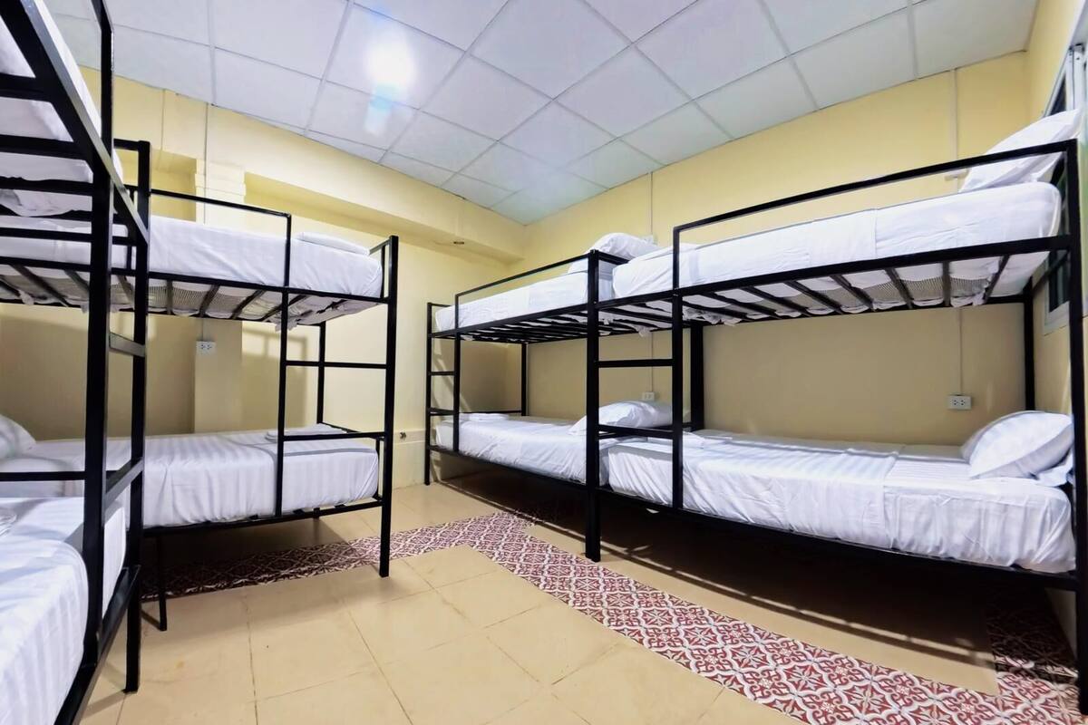 A dormitory room with bunk beds, a patterned rug, and a tiled floor.