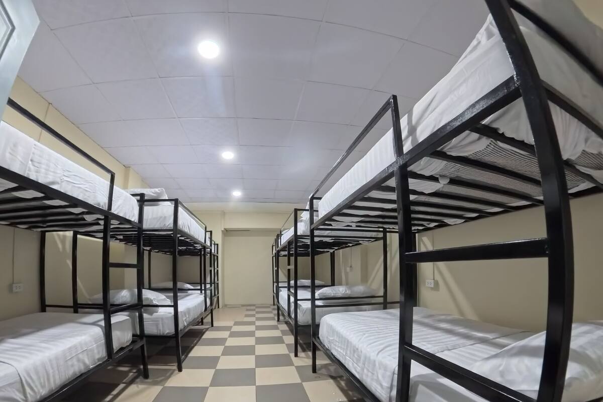 A dormitory room with bunk beds arranged in two rows, a checkered floor, and a ceiling with recessed lighting.