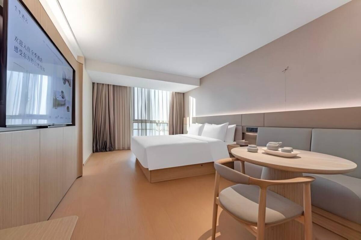 A modern hotel room with a bed, bedside table, and a large screen on the wall.