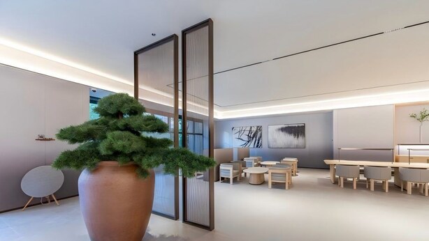 Un interior moderno con un gran árbol en maceta, una zona de comedor con mesas redondas y un diseño minimalista.