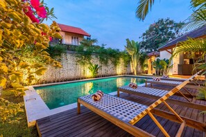 Un espace aménagé au bord de la piscine, avec des chaises longues, un mur en pierre et un bâtiment doté d’un toit rouge.