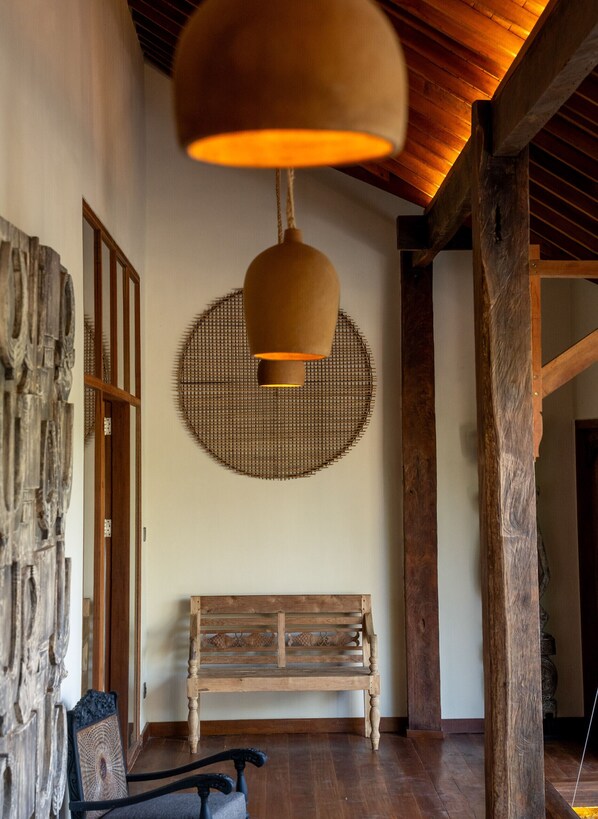 Un banc en bois placé sous un luminaire suspendu, dans une pièce dotée d’un plafond en bois et d’une tapisserie murale tissée.