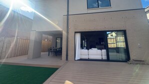 Una casa moderna de dos pisos con un patio, un comedor y un amplio ventanal corredizo que da a un espacio interior.