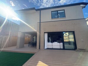 A modern two-story house with a patio, a dining area, and a large sliding glass door leading to an interior space. - Luxury Escape (Clyde North)