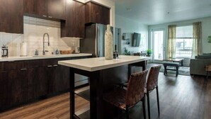 A modern kitchen with dark wood cabinets, a white countertop, and a central island with chairs. - Clean Cozy and Calm Retreat (Glendale)