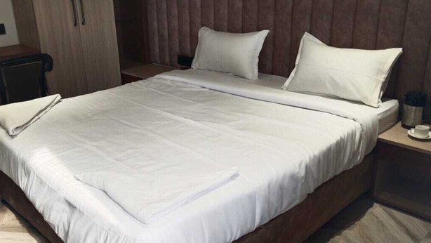 Un letto ben rifatto con lenzuola bianche, una testiera in legno e un comodino con tazza e piattino.
