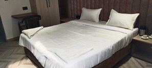 A neatly made bed with white linens, a wooden headboard, and a bedside table with a cup and saucer. - Hotel B K Stay (Mainpuri)