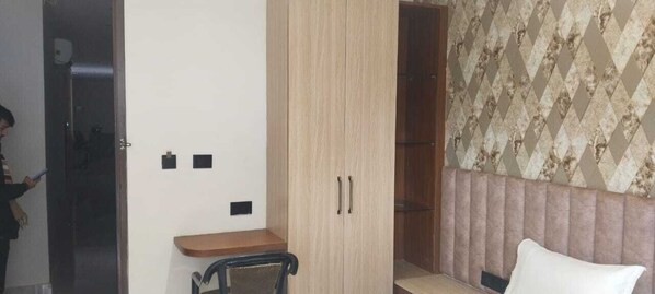 A room with a wooden wardrobe, a small table, a chair, and a patterned wall. - Hotel B K Stay (Mainpuri)