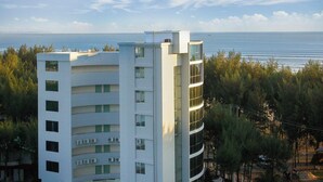 Ein mehrstöckiges Gebäude mit Balkonen, Blick auf das Meer und einer bewaldeten Landschaft im Hintergrund.