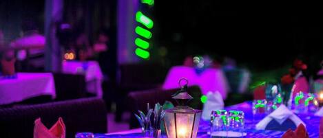 Une table dressée pour le dîner, avec une nappe à motifs, des chandeliers et une lanterne allumée.